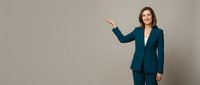 Professional businesswoman in teal suit presenting with open hand gesture against neutral background for corporate and business presentations.