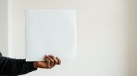 Cropped view of hand holding blank white paper sheet against neutral background for mockup and branding projects.