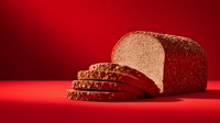 Freshly sliced whole grain bread loaf on vibrant red background, showcasing texture and nutritional appeal for food marketing.