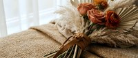 Autumn wedding bouquet with dried roses, pampas grass and wheat stems tied with ribbon on textured fabric background for rustic ceremony decor.