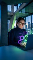 Professional businesswoman working on laptop with holographic digital technology interface in modern office building at night.
