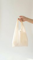 Hand holding eco-friendly reusable cotton tote bag on neutral background for sustainable shopping and zero waste lifestyle concept.