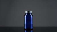 Blue glass pharmaceutical bottle with silver cap on dark background for medical packaging and supplement branding.