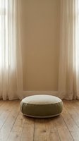 Minimalist beige round floor cushion on wooden floor with natural light filtering through sheer curtains creating warm atmosphere for meditation and relaxation.