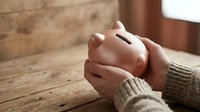 Hands holding pink piggy bank on wooden table, savings and financial planning concept for personal budget management and money investment goals.