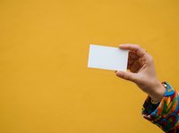 Close-up of a hand holding a blank white card against a bright yellow background. Ideal for business card mockups, contact information displays, and promotional material presentations.