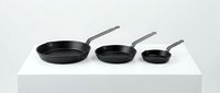 Set of three black nonstick frying pans with stainless steel handles in decreasing sizes, displayed on white surface for kitchenware retail and cooking product promotion.