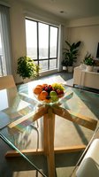 Modern dining room with glass table, wooden base, and fresh fruit bowl, featuring floor-to-ceiling windows, potted plants, and natural sunlight for interior design and home decor projects.