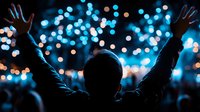 Silhouette of person with raised arms against blurred blue bokeh lights at night concert or festival, creating atmospheric celebratory mood.
