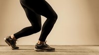 Athlete in black leggings and sneakers performing dynamic running motion against neutral background for fitness, sports, and wellness marketing materials.