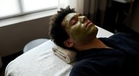 Young African American man relaxing with green facial mask during spa treatment at wellness center. Self-care skincare routine for healthy glowing skin.