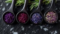 Colorful dried herbs and spices in wooden spoons on dark slate background. Natural organic seasonings for cooking and culinary applications.