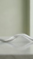 Silky white hair strand flowing in smooth wave pattern on neutral surface, isolated against soft blurred background, suitable for beauty, haircare, and cosmetic product design use.