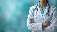 Asian female medical professional in white coat and stethoscope standing with crossed arms against blurred teal background, representing healthcare and medical expertise.