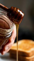 Honey dripping from wooden dipper into glass jar with toast in background, perfect for food and beverage marketing, cooking blogs, and breakfast content.