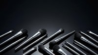 Professional makeup brushes with silver handles arranged on dark background, top view with copy space for beauty and cosmetics design.