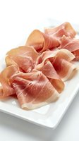 Thin slices of cured ham arranged on white ceramic plate, premium deli meat for gourmet cooking, charcuterie boards and culinary presentations.