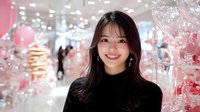 Young Asian woman smiling warmly in black turtleneck against blurred festive pink background with bokeh lights and holiday decorations, portrait with soft dreamy atmosphere.