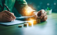 Businessman calculating mortgage loan with house icon hologram and coins on desk for real estate investment planning and financial analysis.