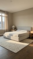 Serene bedroom interior with upholstered platform bed, natural linen bedding, wooden nightstands, layered area rugs, and floor-to-ceiling windows with sheer curtains allowing soft natural light.