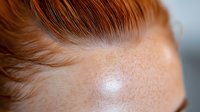 Close up portrait showing natural freckles and ginger hair against soft blurred background, highlighting skin texture and warm tones for beauty and cosmetic advertising.