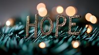 Glittery letters spelling HOPE placed on pine branches with soft bokeh lights creating magical holiday atmosphere against dark background.