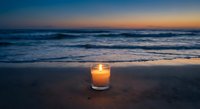 Glowing candle on sandy beach at twilight with ocean waves and colorful sunset sky creating peaceful meditation atmosphere for relaxation and mindfulness.