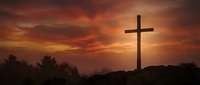 Wooden cross silhouetted against dramatic sunset sky with orange and red clouds on hilltop, symbolizing faith, hope, and spiritual devotion for religious content.