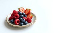 Mixed fresh berries including raspberries, blueberries and strawberries arranged on a ceramic plate against white background for food styling and culinary design.