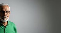Senior man with gray hair and beard wearing glasses and green shirt against neutral background, suitable for healthcare, business, and lifestyle editorial use.