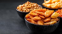 Assorted salty snacks and nuts in black bowls on dark background with copy space. Crunchy party mix of roasted peanuts and crackers for appetizer.