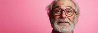 Happy senior Caucasian man with gray beard and glasses smiling warmly against pink background. Elderly gentleman expressing joy and positivity for lifestyle content.
