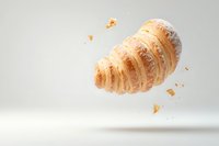Fresh buttery croissant floating in air with crumbs scattered around on light background, powdered with sugar. Food photography for bakery and cafe promotion.