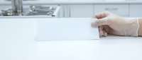 Hand in protective latex glove reaching for white business card on clean laboratory counter surface for medical professional branding mockup.