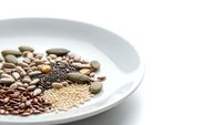 Assorted legumes and seeds arranged on white ceramic plate including lentils quinoa beans and pumpkin seeds for healthy cooking and nutrition.