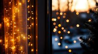 Glowing fairy lights create magical atmosphere near window at dusk, with bokeh effect and Christmas tree silhouette, bringing cozy winter holiday ambiance.