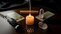 Mystical tarot reading setup with burning candle, crystals, incense smoke and pentagram symbol on dark wooden surface for spiritual guidance.