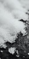 Macro photography of delicate snow crystals and frost formations on dark surface creating dramatic contrast between white ice structures and black background.