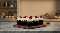 Chocolate cupcakes with vanilla frosting and raspberry garnish on wooden board in modern kitchen setting for bakery and dessert photography.