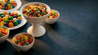 Colorful candy assortment in ceramic bowls on dark wooden table for party celebrations and sweet treats display.