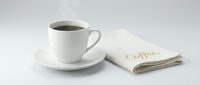 Hot steaming black coffee in a white ceramic cup on saucer beside a linen napkin with gold script lettering on light background.