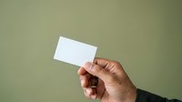 Cropped hand holding blank white business card against neutral sage green background, ready for branding and corporate identity design mockups.