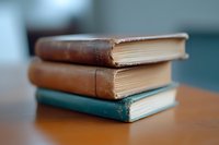 Stack of vintage worn books with leather covers and aged pages on wooden surface against blurred teal background, creating nostalgic academic atmosphere.