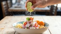 Hand squeezing fresh lime juice over ceviche with shrimp, corn, and red onion in white bowl on wooden table for seafood recipe.