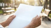 Senior man holding blank white paper outdoors in sunny park setting, suitable for advertising, marketing materials, and promotional campaigns.
