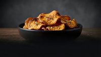 Crispy homemade potato chips with herbs and spices served in black bowl on wooden table against dark background for snack food advertising.