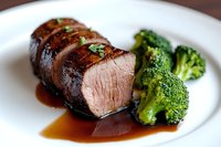 Juicy sliced pork tenderloin with caramelized glaze served alongside steamed broccoli florets on white plate, showcasing medium-rare doneness and rich sauce.