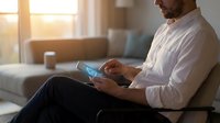 Professional businessman using smartphone in modern living room with warm sunlight streaming through windows during golden hour.