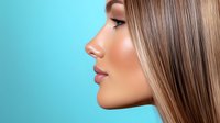 Side profile of young woman with glowing skin and straight blonde hair against turquoise background, highlighting natural beauty and facial features in modern beauty portrait.