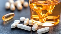 Prescription pills scattered near glass of alcohol with skull shape, highlighting dangers of mixing medications and drinks. Medical warning concept.